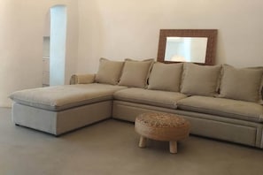 A L-shaped sectional sofa with a matching ottoman, a mirror with a brick frame, and a white wall. - Villa LuxL Winery Villa (Mesaria)