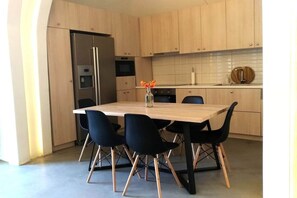 A modern kitchen with a central island, black chairs, and a stainless steel refrigerator. - Villa LuxL Winery Villa (Mesaria)