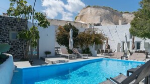 Piscina con sillas de descanso y sombrillas, rodeada por un muro de piedra y vegetación.