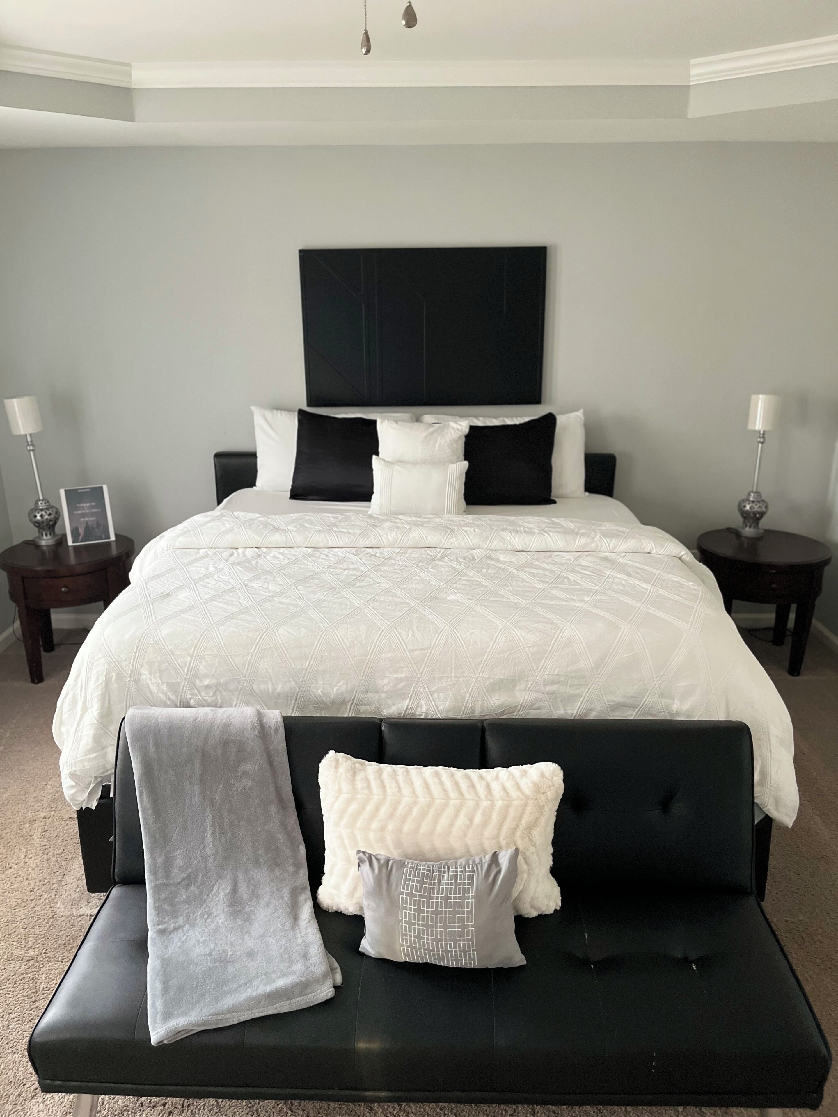 A bedroom with a large bed, two bedside tables, a headboard, and a bench with cushions.
