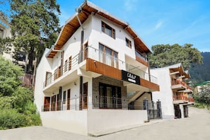 Un edificio de dos pisos con un balcón, un letrero que indica que es una colección de servicios para empresa, y vistas de la vegetación y colinas circundantes.
