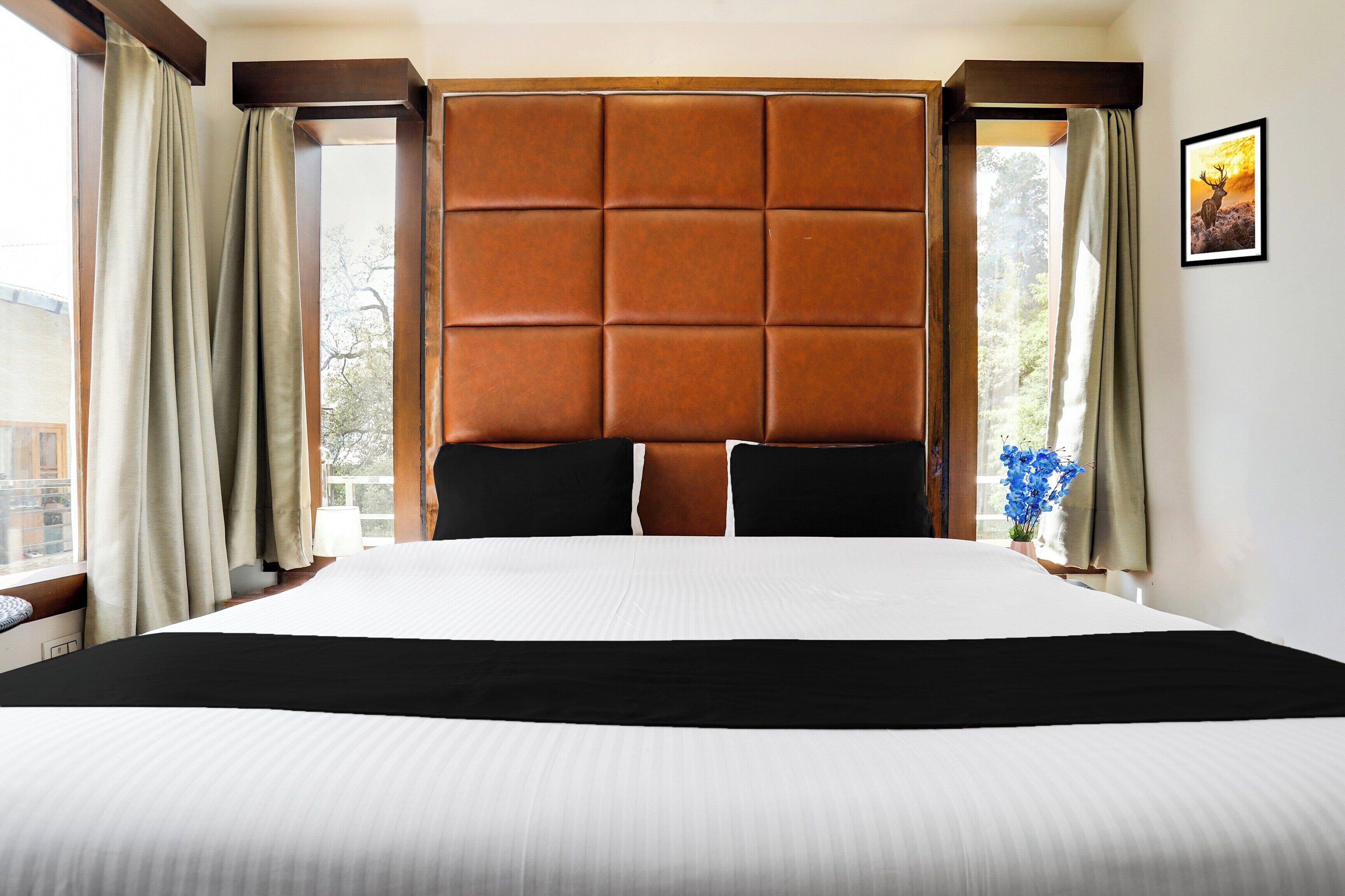 Una habitación de hotel con una cama grande, un cabecero acolchado y cortinas en las ventanas.