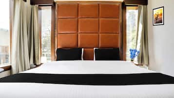 Una habitación de hotel con una cama grande, un cabecero acolchado y cortinas en las ventanas.