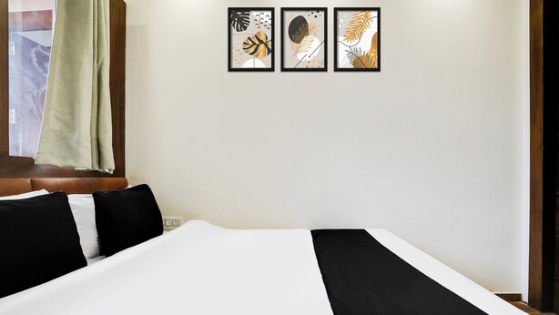 A hotel room with a bed, a window with a curtain, and three framed artworks on the wall.