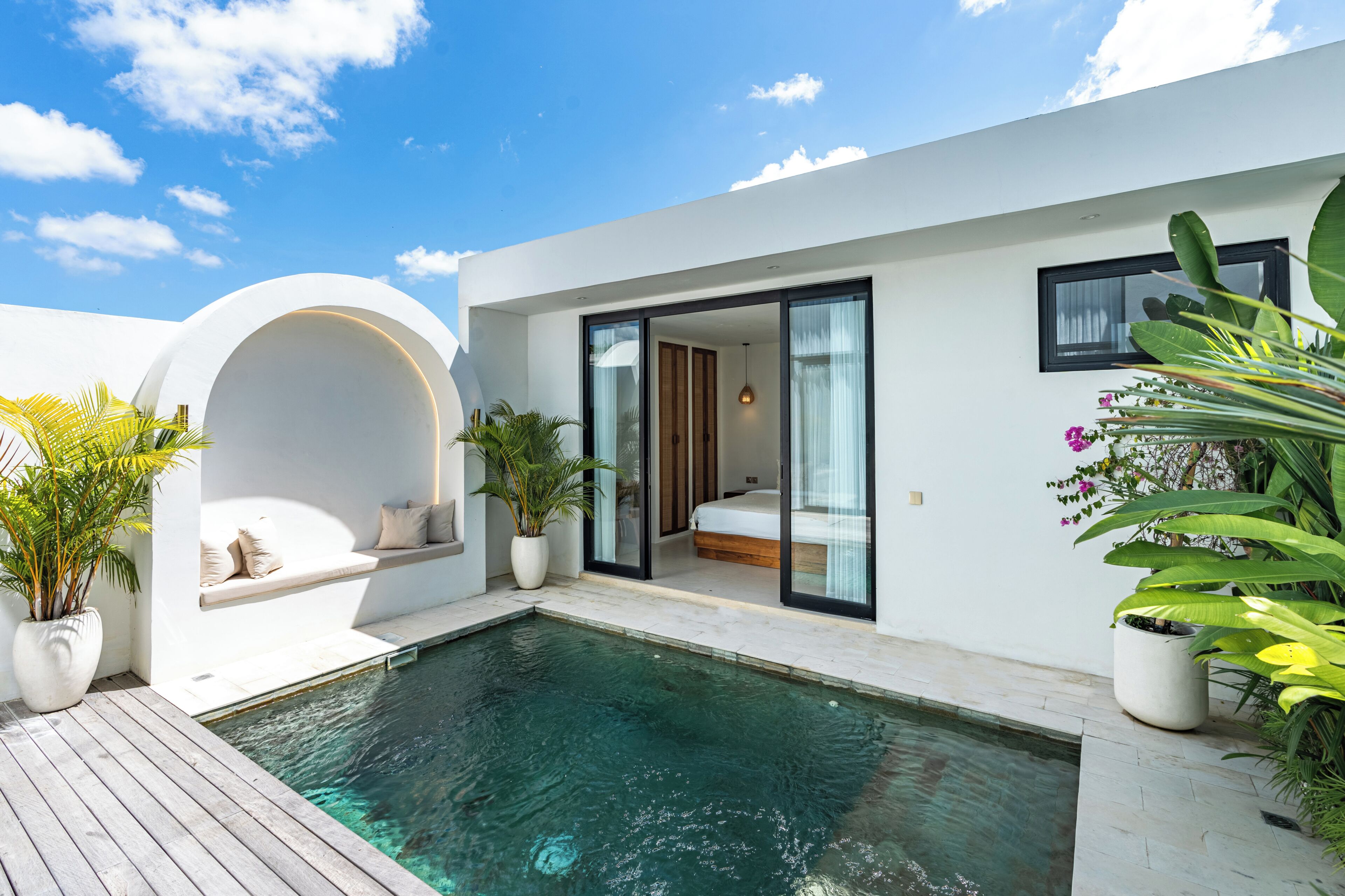 A modern house with a swimming pool, a glass door leading to a bedroom, and potted plants.
