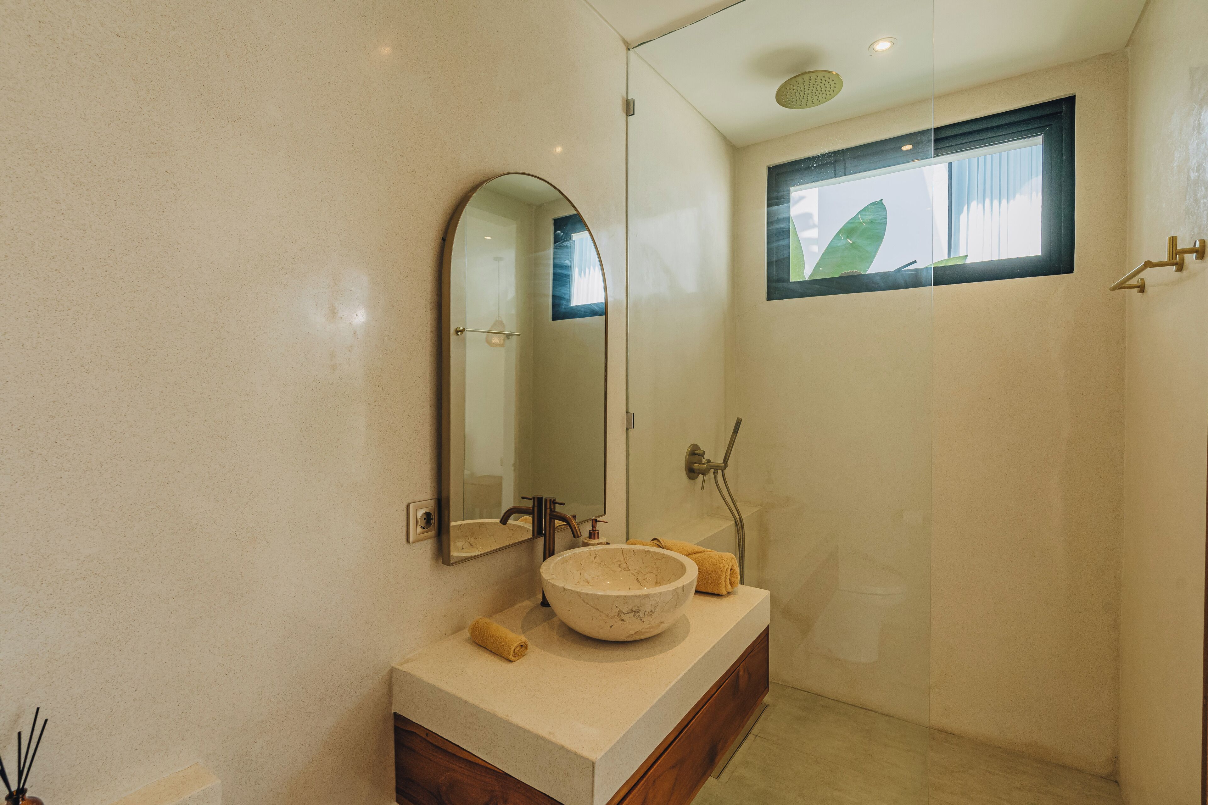 Un baño con un lavamanos ovalado grande, un espejo, una ventana y una zona de ducha.