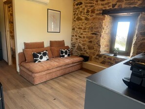 A cozy living room with a stone wall, a sofa with patterned cushions, and a window with natural light.