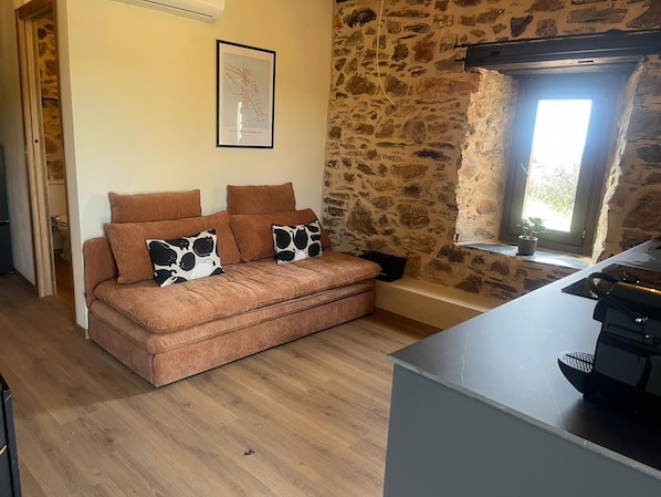 A cozy living room with a stone wall, a sofa with patterned cushions, and a window with natural light.