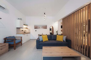 A modern living room with a dark sofa, wooden coffee table, and a kitchen in the background. - Ag. Ma Maria Suite - Chalkidiki w/ Priv Parking (Nikiti)