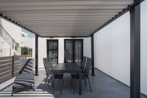 An outdoor patio with a table and chairs, a covered area, and a view of a building in the background. - Ag. Ma Maria Suite - Chalkidiki w/ Priv Parking (Nikiti)
