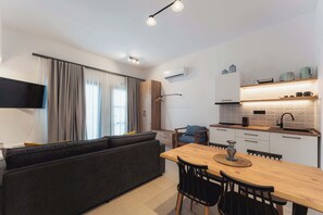 A modern kitchen with a dining area, a sofa, and a TV mounted on the wall. - Ag. Ma Maria Suite - Chalkidiki w/ Priv Parking (Nikiti)