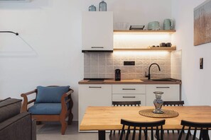 A modern kitchen with white cabinets, a wooden dining table, and a blue chair. - Ag. Ma Maria Suite - Chalkidiki w/ Priv Parking (Nikiti)