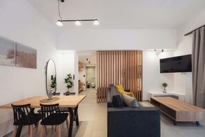 Uma sala de estar moderna com área de jantar, sofá, TV e um painel de madeira.