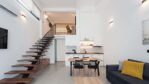 A modern apartment with a wooden staircase, a dining area, a kitchen, and a living room with a sofa and a yellow pillow. - Ag. Ma Aggelos Suite - Chalkidiki w/ Priv Parking (Nikiti)