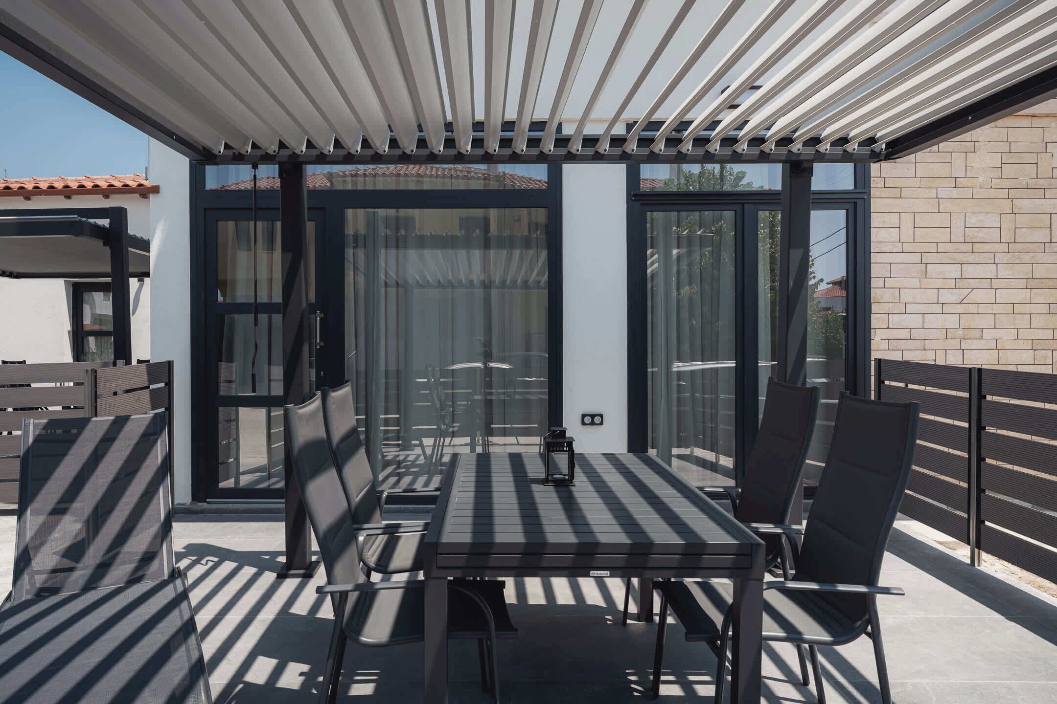 An outdoor patio with a table and chairs, a pergola overhead, and a glass door leading to a covered area.