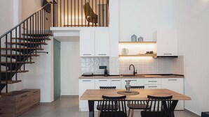 A modern kitchen with a wooden dining table, black chairs, and a staircase with a railing. - Ag. Ma Aggelos Suite - Chalkidiki w/ Priv Parking (Nikiti)