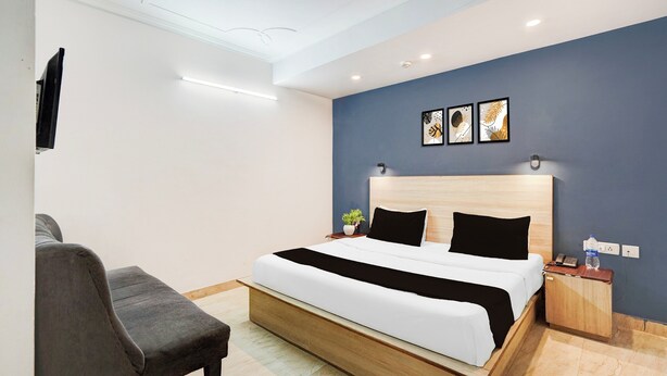 Habitación de hotel con cama, escritorio, silla, mesita de noche, televisión montada en la pared y obra de arte.