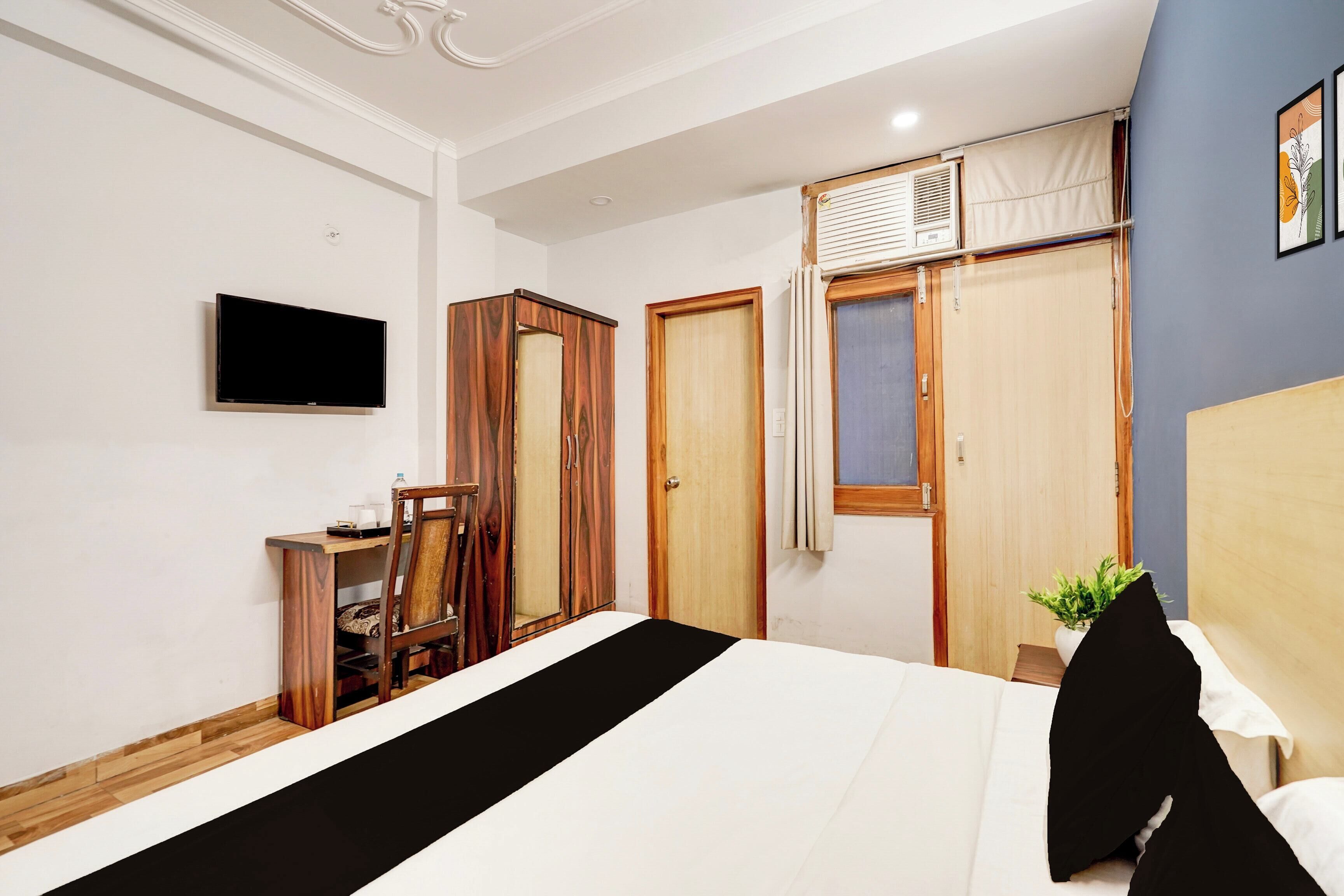 Quarto com cama, televisão, guarda-roupa e janela com cortinas.