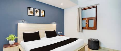 Habitación de hotel con cama, mesita de noche, planta en maceta y ventana con cortinas.