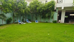 Un espace extérieur verdoyant avec trois chaises longues et un mur blanc orné d’arbres.