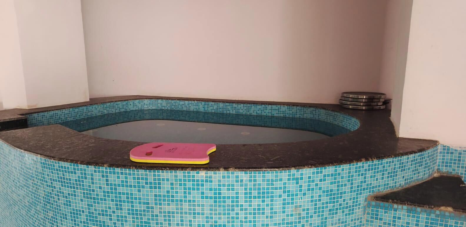 A hot tub with a pink mat, surrounded by a tiled pool.