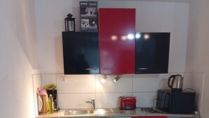 A compact kitchen with a glass dining table, red and black cabinets, a coffee maker, and a toaster.