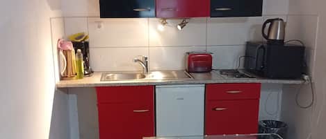 A compact kitchen with a glass dining table, red and black cabinets, a coffee maker, and a toaster.