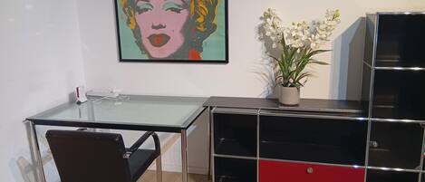 A modern room with a glass desk, a red and black cabinet, a potted plant, and a pop art painting on the wall.
