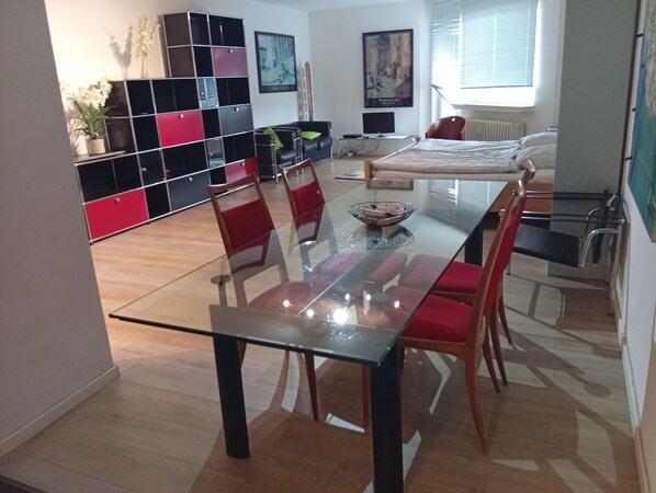 Una sala moderna con una mesa de comedor de vidrio, sillas rojas, un sofá y un estante negro y rojo.
