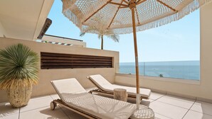 A sunlit balcony with two lounge chairs, a large potted plant, and a view of the sea. - RDR574 Beachfront Luxury 4-Bed Penthouse in Velaya (Estepona)