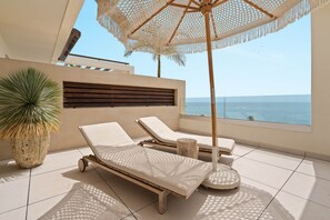 Ein sonniger Balkon mit zwei Liegestühlen, einem großen Kübelpflanzen und Blick aufs Meer.