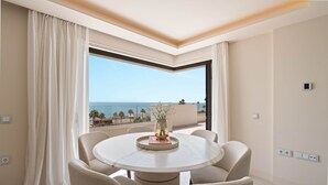 A round dining table with six chairs, a vase with a plant, and a view of the sea through a large window. - RDR574 Beachfront Luxury 4-Bed Penthouse in Velaya (Estepona)