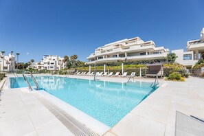 Une piscine avec des chaises longues, un espace de repos couvert et des bâtiments modernes en arrière-plan.