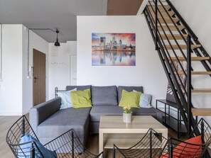 A modern living room with a grey sectional sofa, a coffee table, and a staircase with black railings. - Elegant Central City Apartment in Warsaw (Warsaw)
