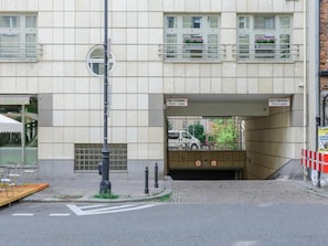 Ein Gebäude mit Fliesenfassade, einer Fußgängerampel, Leitpfosten und einem Straßenschild.