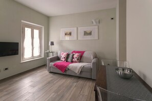 A living room with a sofa, a coffee table, a TV, and a window. - Locanda della Porta 1 (Guastalla)
