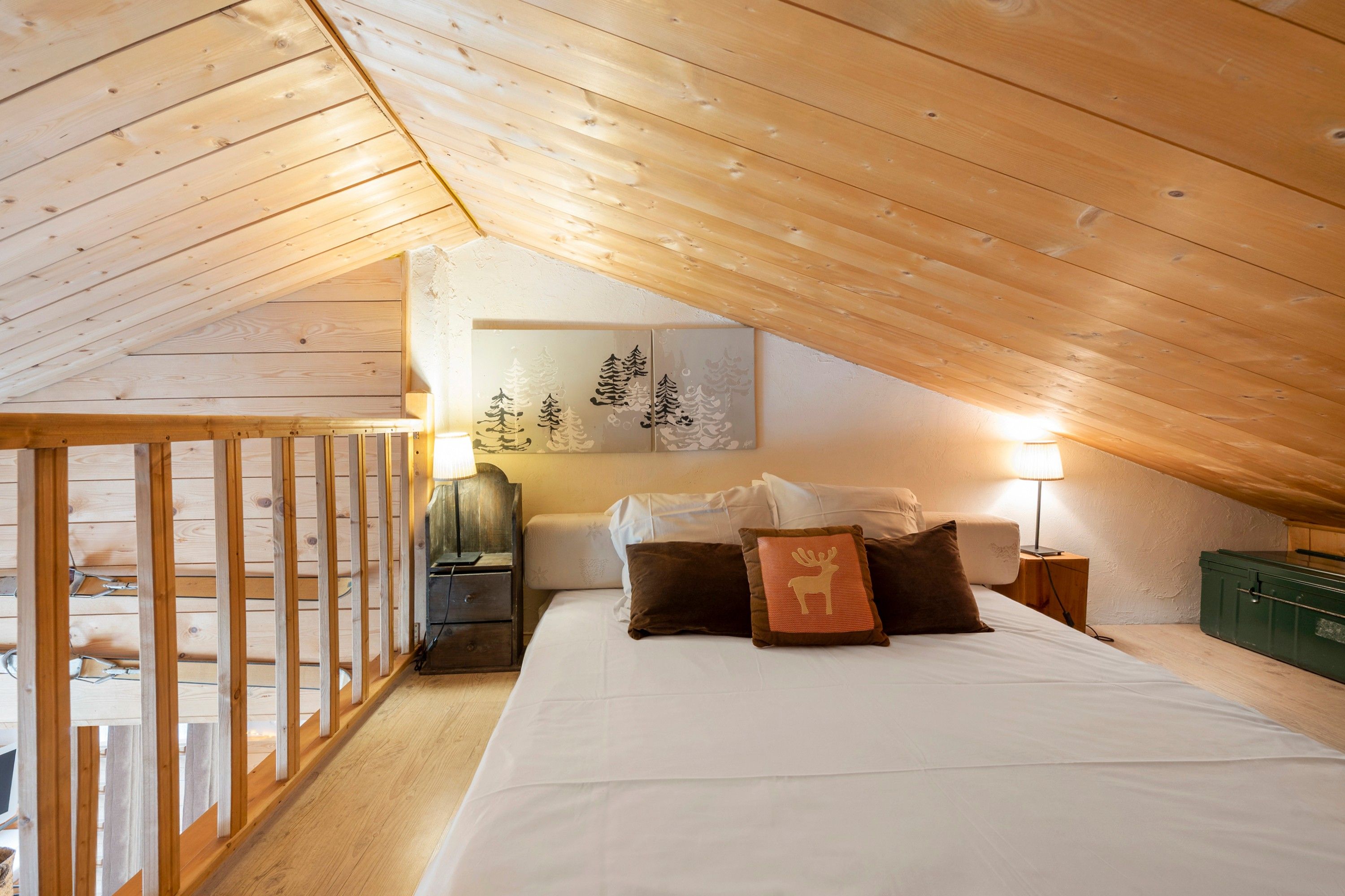 Une chambre avec un plafond en pente, un lit avec des oreillers, une table de chevet, une lampe et une œuvre d’art accrochée au mur.