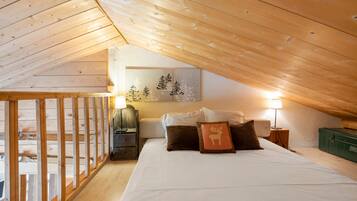 Une chambre avec un plafond en pente, un lit avec des oreillers, une table de chevet, une lampe et une œuvre d’art accrochée au mur.