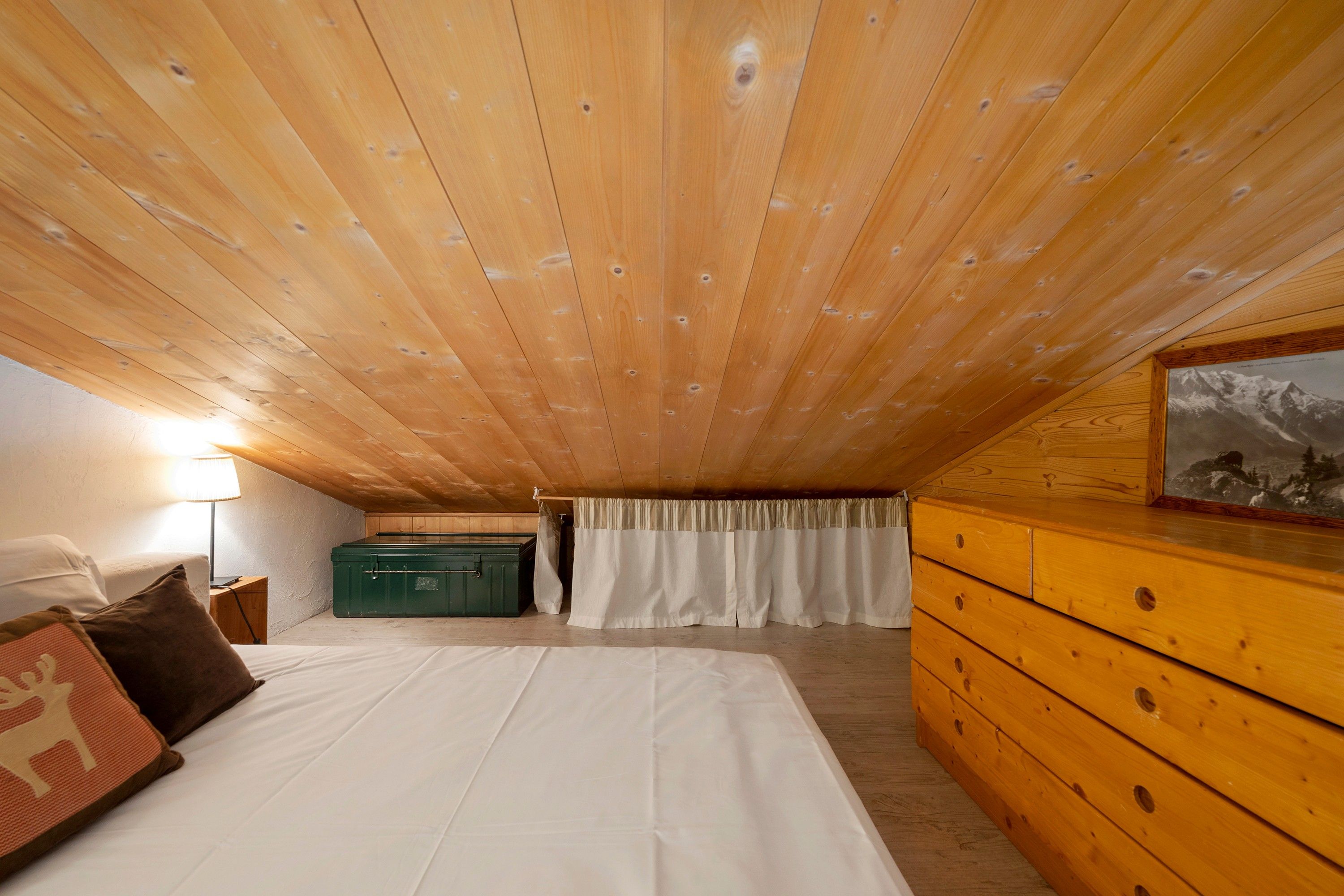 Een slaapkamer met een houten plafond, een bed, een kaptafel, een groene dressoir en een schilderij aan de muur.