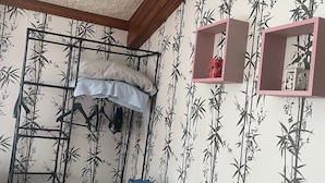 Een kamer met een stapelbed, een houten tafel en een blauwe stoel. Twee roze planken met decoratieve spullen.