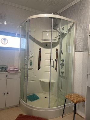 A corner shower enclosure with a glass door, a small sink, and a towel rack.