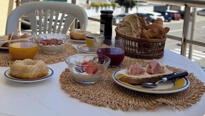 Una mesa servida con alimentos para el desayuno, como pan, pasteles y una bebida, en un balcón con vistas a edificios.
