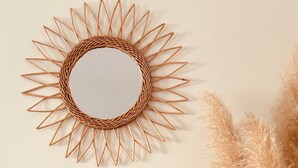 Un espejo con forma de sol montado en la pared, con un centro circular y elementos de madera que se extienden hacia afuera.