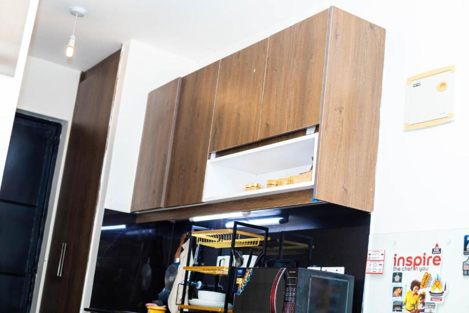 A kitchen with wooden cabinets, a microwave, and a shelf with jars.