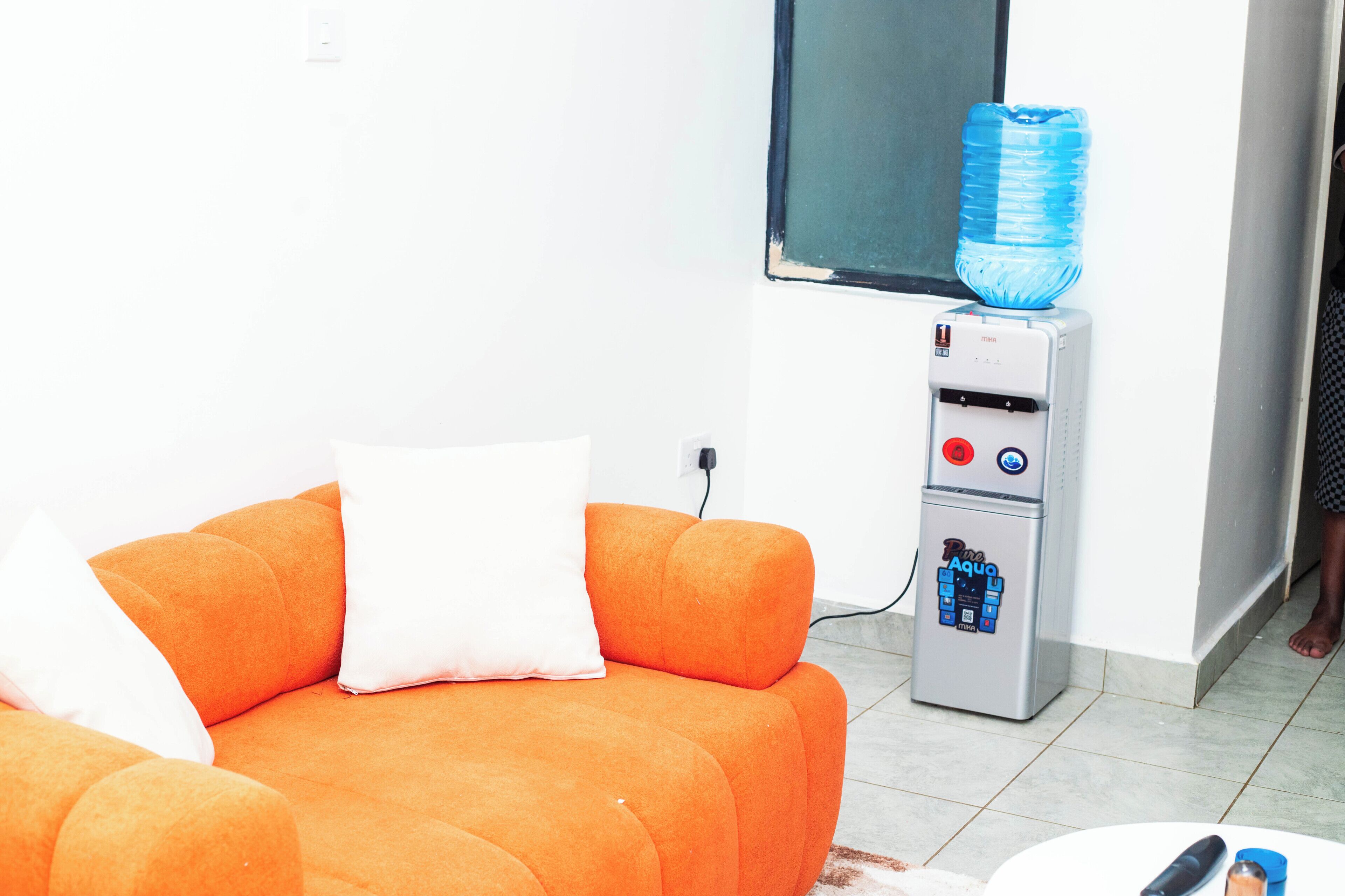 Een kamer met een oranje bank, een waterdispenser en een raam.