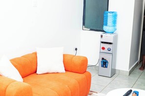 Quarto com sofá laranja, dispensador de água e janela.