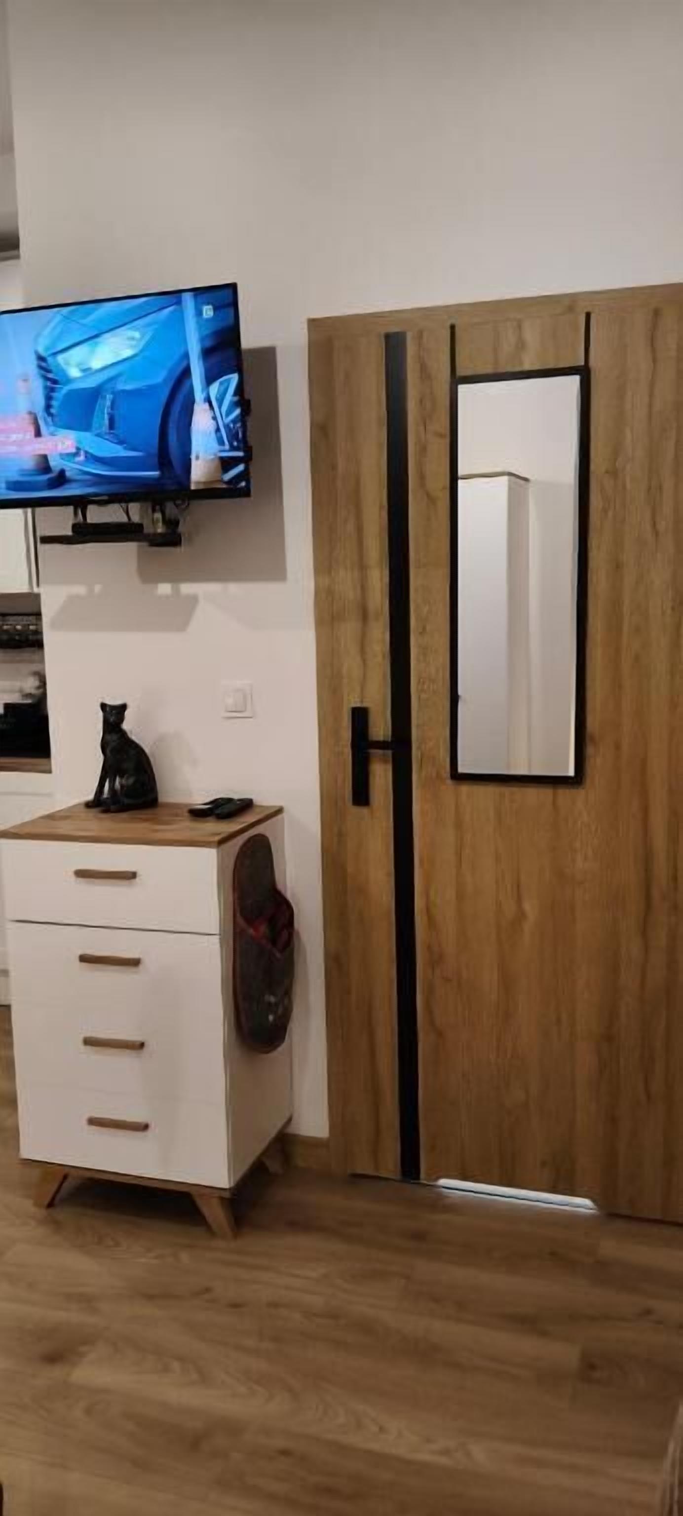Ein Zimmer mit an der Wand befestigtem Fernseher, einem Holzschrank mit Spiegel und einer weißen Kommode mit Schubladen.