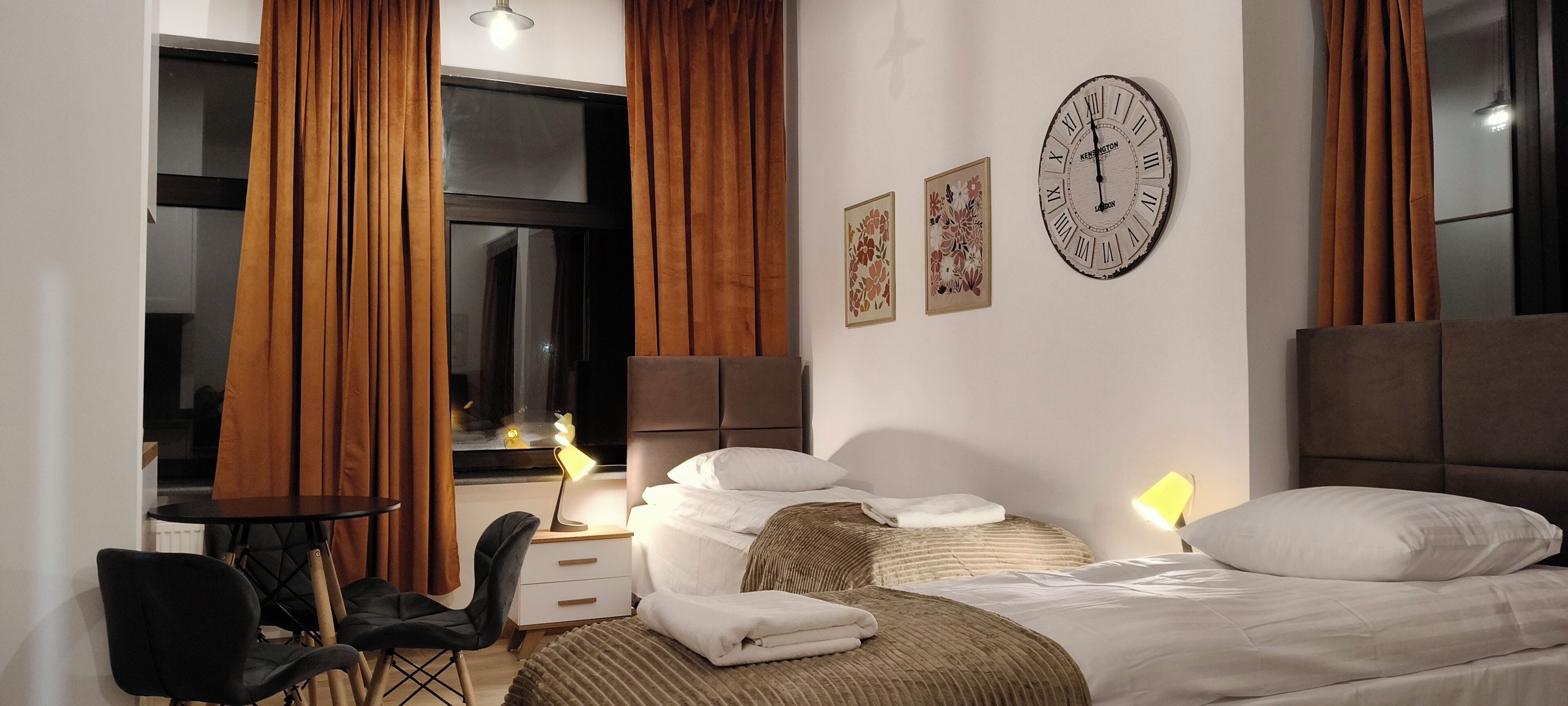 Ein Hotelzimmer mit Bett, Schreibtisch, Stuhl, einem Fenster mit Vorhängen und Wandbildern.