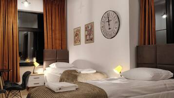 Ein Hotelzimmer mit Bett, Schreibtisch, Stuhl, einem Fenster mit Vorhängen und Wandbildern.