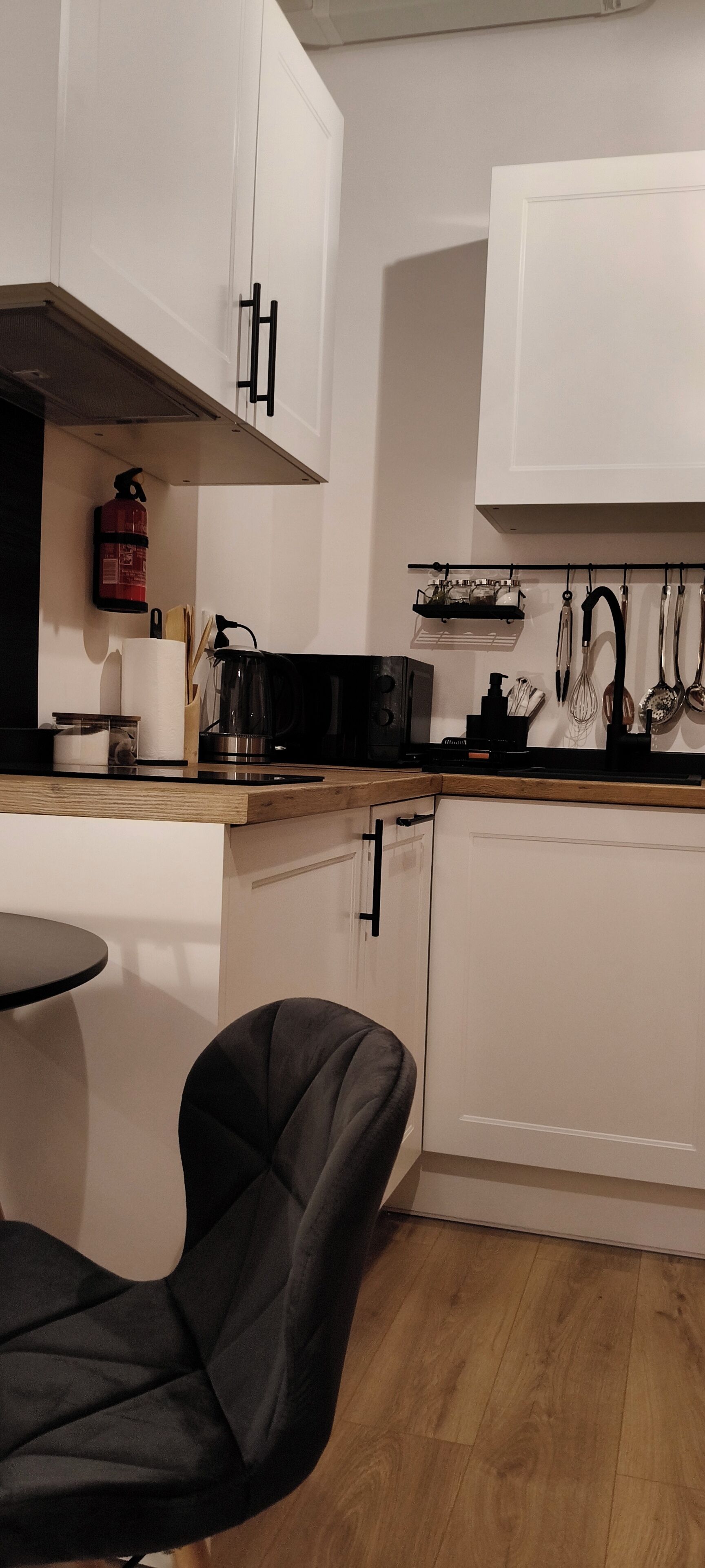 Une cuisine de taille réduite avec des meubles blancs, une chaise noire et une petite table à manger.